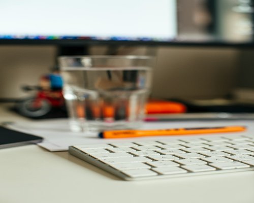 A notebook and pen lying open on a neat desk beside a clean glass of natural water
